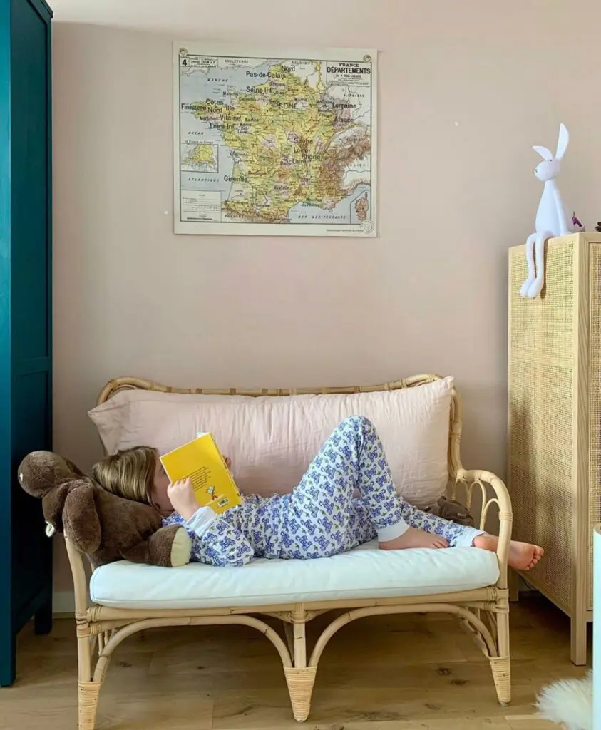 Enfant lisant sur une banquette en rotin, la planche "Carte de France Vidal Lablache" accrochée au mur.
